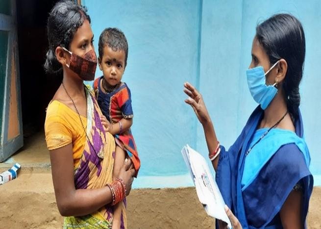 An ASHA worker conducting a home health check-up for a newborn and mother.